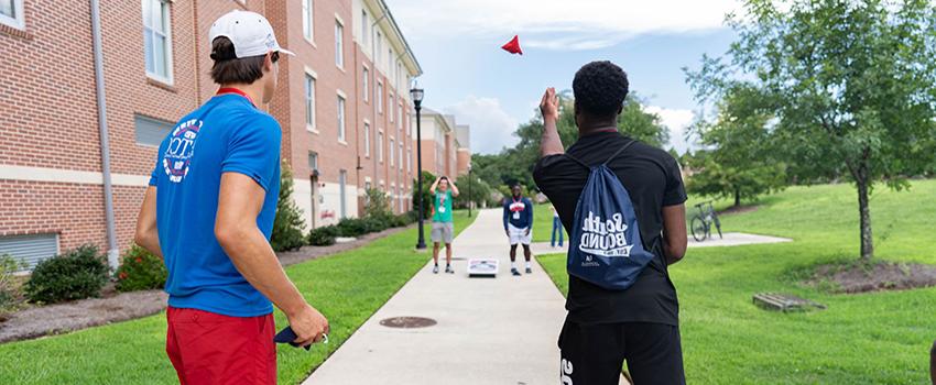 Students playing cornhole outside campus housing.